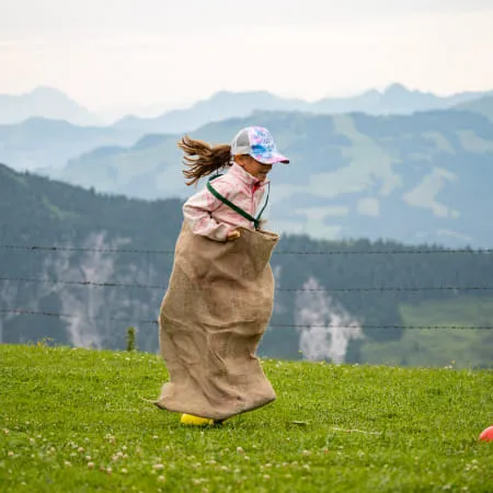 Mädchen springt in einem Sack auf einer Wiese im Brixental